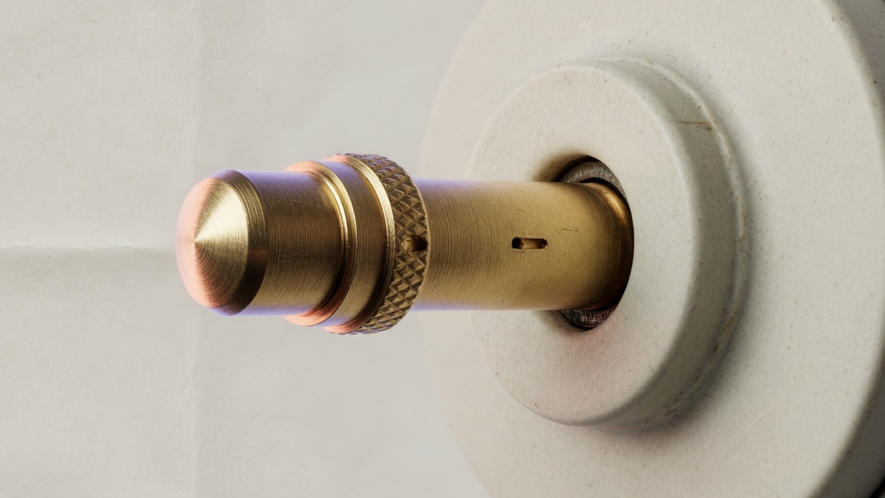 A brass connector pin seated in a pale ceramic socket, photographed in macro against off-white paper